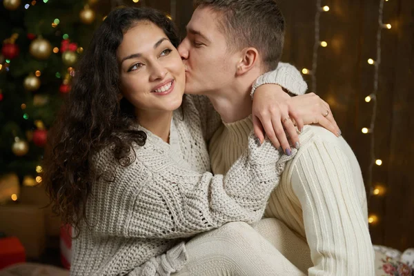 Ζευγάρι σε Χριστουγεννιάτικα φωτάκια και διακόσμηση, ντυμένοι στα λευκά, νεαρό κορίτσι και man, έλατο σε σκούρο φόντο ξύλινη, χειμερινές διακοπές έννοια — Φωτογραφία Αρχείου