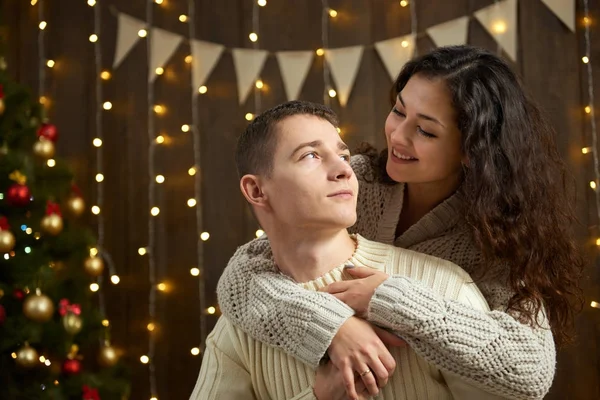 Coppia in luci di Natale e decorazione, vestito di bianco, giovane ragazza e uomo, abete su sfondo di legno scuro, concetto di vacanza invernale — Foto Stock