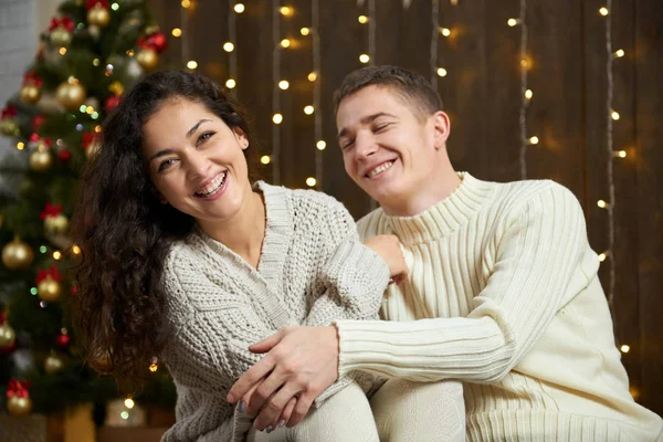 Casal em luzes de Natal e decoração, vestido de branco, jovem e homem, abeto em fundo de madeira escura, conceito de férias de inverno — Fotografia de Stock