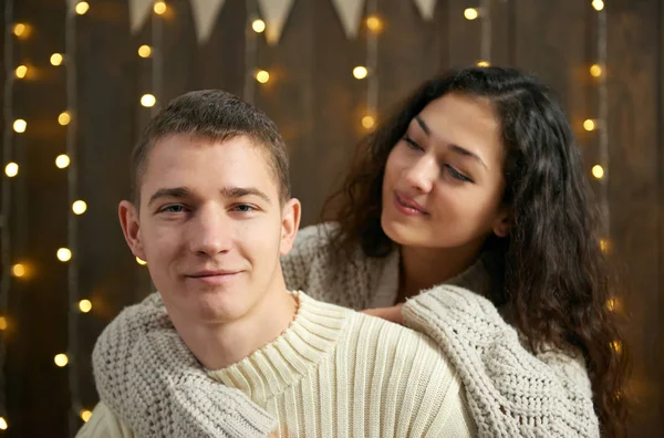 Casal em luzes de Natal e decoração, vestido de branco, jovem e homem, abeto em fundo de madeira escura, conceito de férias de inverno — Fotografia de Stock