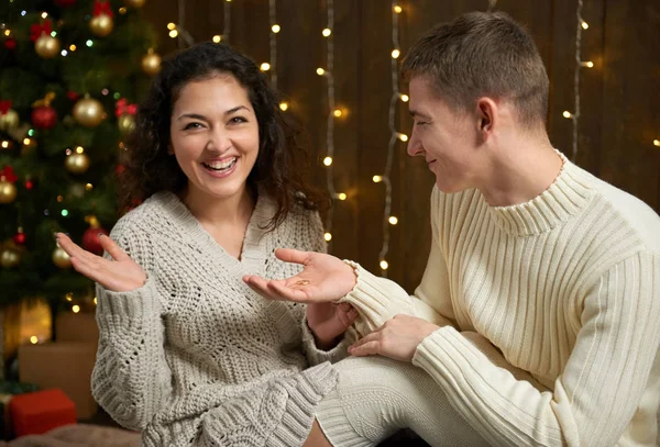 Чоловік дарує дівчині обручку, пару в різдвяних вогнях і прикрасах, одягнену в біле, ялинове дерево на темному дерев'яному фоні, концепція зимових свят — стокове фото