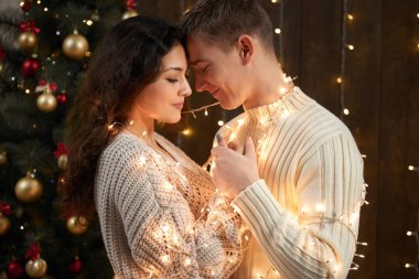 Genç çift birlikte Noel ışıkları ve Dekorasyon, giyinmiş beyaz, koyu ahşap arka plan, romantik akşam, kış tatil kavramı köknar ağacı