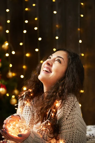 Dívka s hrst vánoční osvětlení, oblečený v bílém svetru, tmavé dřevěné pozadí, Zimní dovolená concept — Stock fotografie