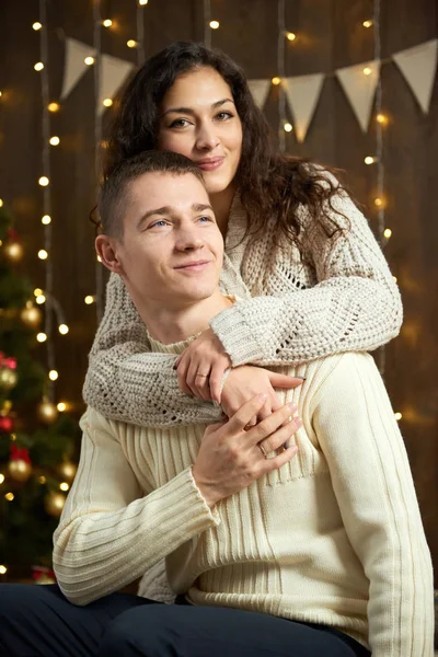 Coppia in luci di Natale e decorazione, vestito di bianco, giovane ragazza e uomo, abete su sfondo di legno scuro, concetto di vacanza invernale — Foto Stock