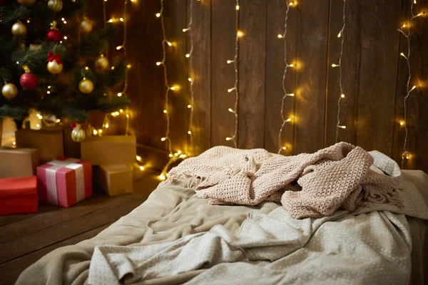 Intérieur de la maison avec mur en bois, lit, arbre de Noël et lumières, concept de vacances d'hiver — Photo