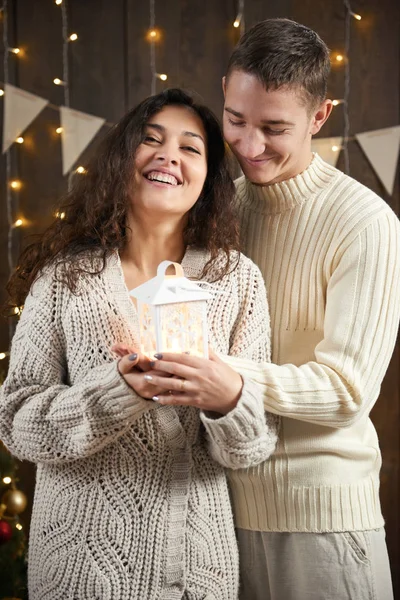 La giovane coppia festeggia il nuovo anno. Luci e decorazioni natalizie. Vestita di maglione bianco. Abete su sfondo di legno scuro, serata romantica, concetto di vacanza invernale — Foto Stock