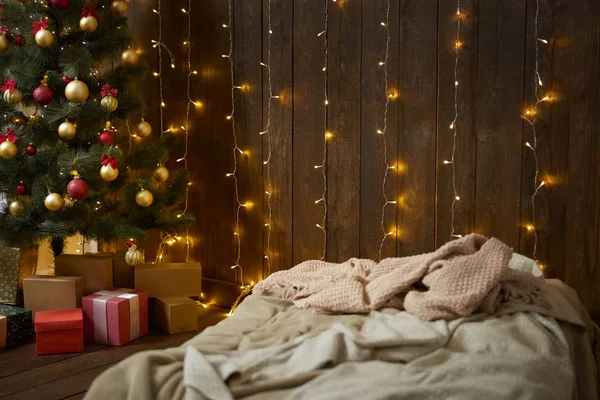 Intérieur de la maison avec mur en bois, lit, arbre de Noël et lumières, concept de vacances d'hiver — Photo