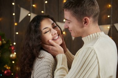 Genç çift koyu ahşap iç ışıkları ile sarılma. Romantik akşam ve sevgi kavramı. Yeni yıl tatili. Noel ışıkları ve dekorasyon. Beyaz giyinmiş.