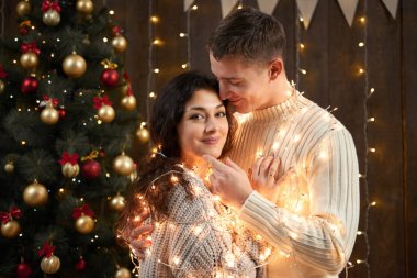 Genç çift birlikte Noel ışıkları ve Dekorasyon, giyinmiş beyaz, koyu ahşap arka plan, romantik akşam, kış tatil kavramı köknar ağacı