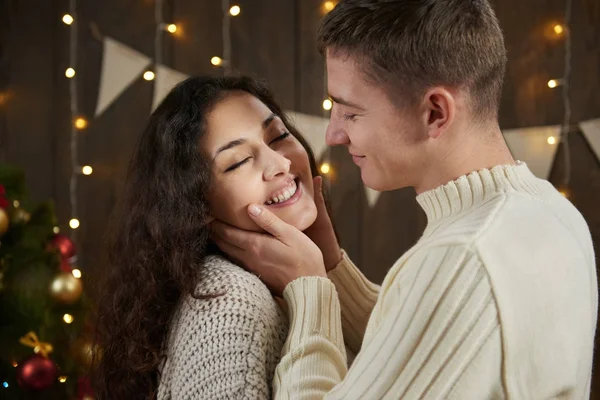 Genç çift koyu ahşap iç ışıkları ile sarılma. Romantik akşam ve sevgi kavramı. Yeni yıl tatili. Noel ışıkları ve dekorasyon. Beyaz giyinmiş.