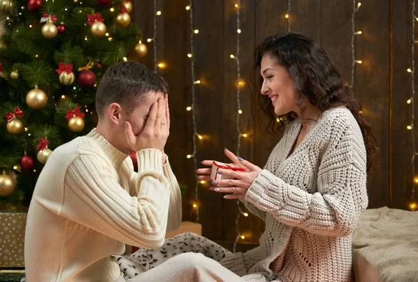 La coppia felice dà regali in decorazione di Natale, sedendosi su pavimento in interno scuro di legno con luci. Serata romantica e concetto d'amore. Vacanza di anno nuovo . — Foto Stock