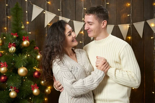Coppia felice posa nella decorazione natalizia, interni in legno scuro con luci. Serata romantica e concetto d'amore. Vacanza di anno nuovo . — Foto Stock