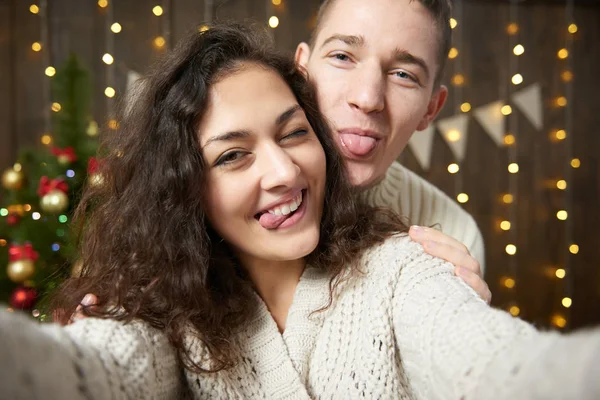 Casal feliz tomando selfie e se divertindo na decoração de Natal. Interior de madeira escura com luzes. Noite romântica e conceito de amor. Férias de Ano Novo . — Fotografia de Stock