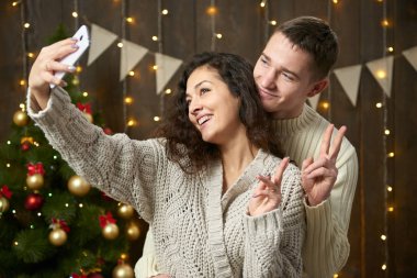 Mutlu çift selfie alarak ve Noel dekorasyonu eğleniyor. Koyu ahşap iç ışıkları ile. Romantik akşam ve sevgi kavramı. Yeni yıl tatili.
