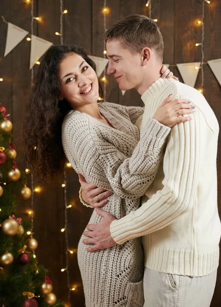 Jong koppel knuffelen in donkere houten interieur met verlichting. Romantische avond en liefde concept. Nieuwjaars vakantie. Kerstverlichting en decoratie. In het wit gekleed. — Stockfoto