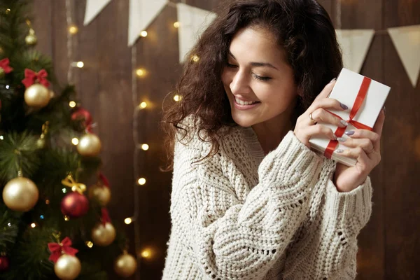 Ευτυχισμένη γυναίκα με δώρο πλαίσιο στην Χριστουγεννιάτικη διακόσμηση. Σκούρα ξύλινα εσωτερικών με φώτα. Ρομαντικό βράδυ και αγάπη έννοια. Αργία Πρωτοχρονιάς. — Φωτογραφία Αρχείου