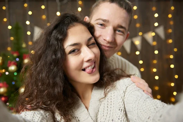 Gelukkige paar selfie te nemen en plezier in Kerstdecoratie. Donkere houten interieur met verlichting. Romantische avond en liefde concept. Nieuwjaars vakantie. — Stockfoto