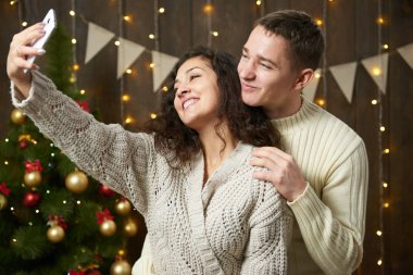 Mutlu çift selfie alarak ve Noel dekorasyonu eğleniyor. Koyu ahşap iç ışıkları ile. Romantik akşam ve sevgi kavramı. Yeni yıl tatili.