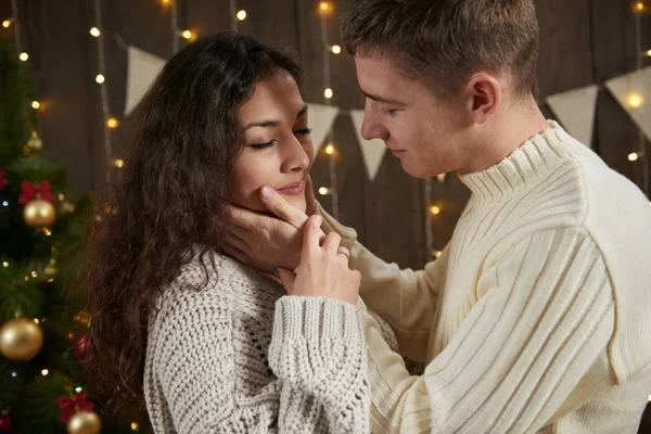 Νεαρό ζευγάρι αγκάλιασμα στο σκοτεινό ξύλινο εσωτερικό με φώτα. Ρομαντικό βράδυ και αγάπη έννοια. Νέο έτος διακοπές. Χριστουγεννιάτικα φωτάκια και διακόσμηση. Ντυμένες στα λευκά. — Φωτογραφία Αρχείου