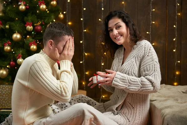 La coppia felice dà regali in decorazione di Natale, sedendosi su pavimento in interno scuro di legno con luci. Serata romantica e concetto d'amore. Vacanza di anno nuovo . — Foto Stock