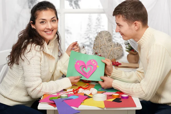 Romantica giovane coppia si siede a tavola e mostra origami cuore rosso, persone felici e concetto di amore — Foto Stock