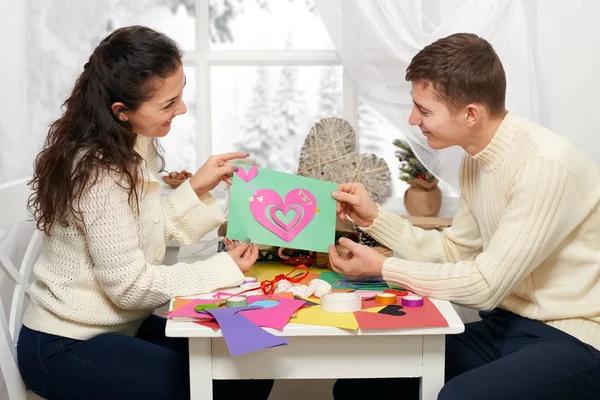 Romantica giovane coppia si siede a tavola e mostra origami cuore rosso, persone felici e concetto di amore — Foto Stock