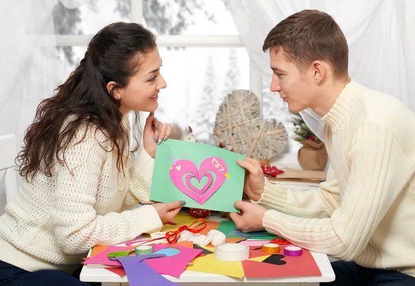 Romantica giovane coppia si siede a tavola e mostra origami cuore rosso, persone felici e concetto di amore — Foto Stock
