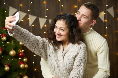 Mutlu çift selfie alarak ve Noel dekorasyonu eğleniyor. Koyu ahşap iç ışıkları ile. Romantik akşam ve sevgi kavramı. Yeni yıl tatili.