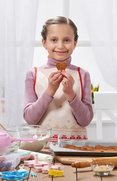 Girl cooking in home kitchen, shows cookies in the shape of a heart, healthy food concept