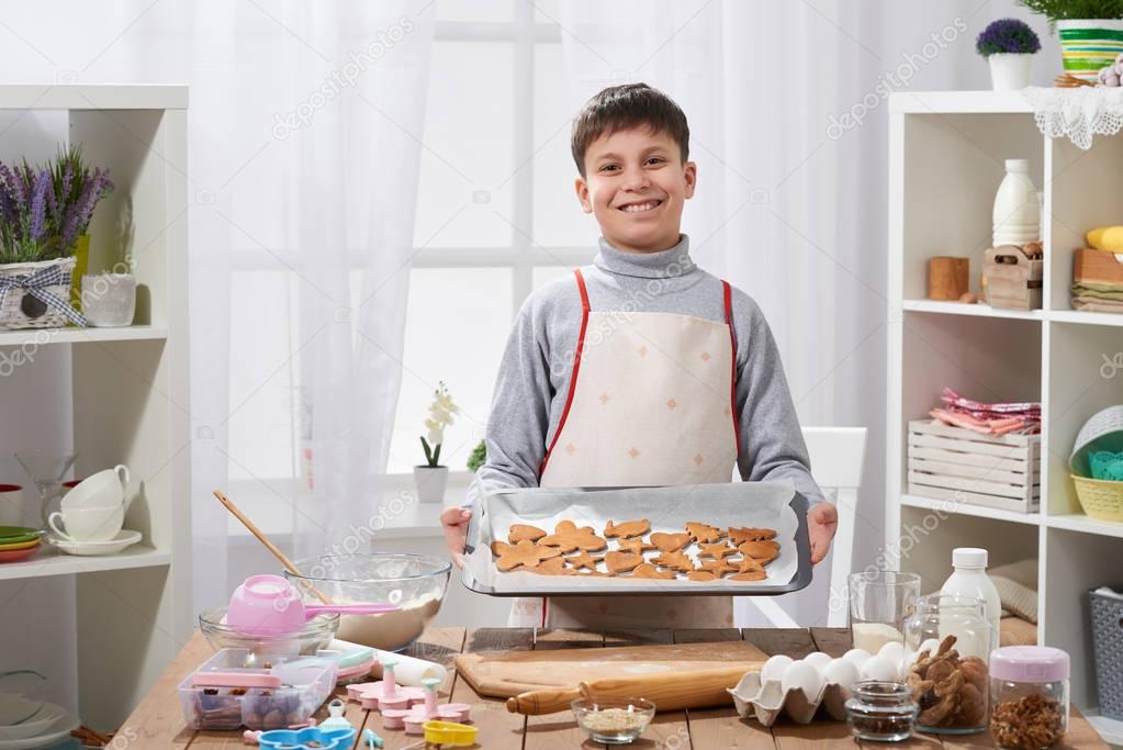 Boy shows a tray of baked cookies in home kitchen interior, homemade food concept