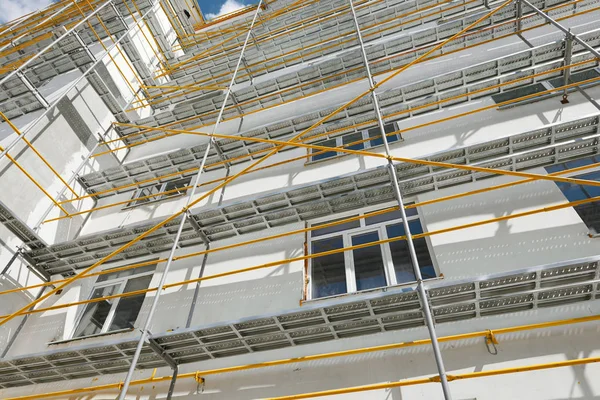 Andaimes perto de uma nova casa, construção exterior, construção e indústria de reparação, parede branca e janela, tubo amarelo — Fotografia de Stock