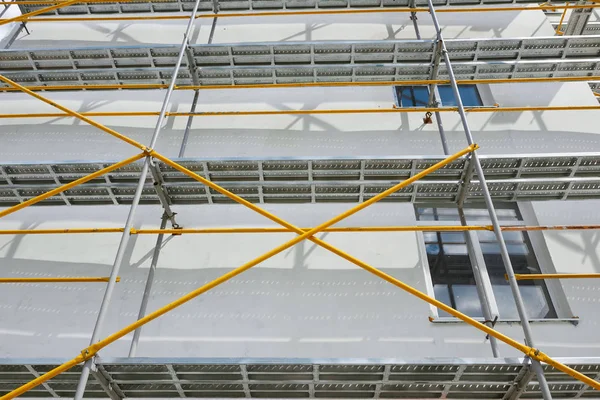 Scaffolding near a new house, building exterior, construction and repair industry, white wall and window, yellow pipe — Stock Photo, Image