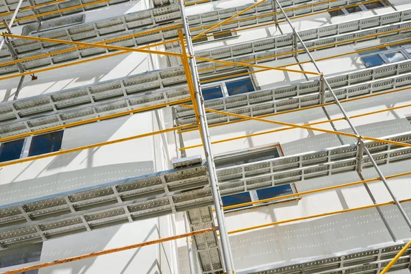 Andaimes perto de uma nova casa, construção exterior, construção e indústria de reparação, parede branca e janela, tubo amarelo — Fotografia de Stock