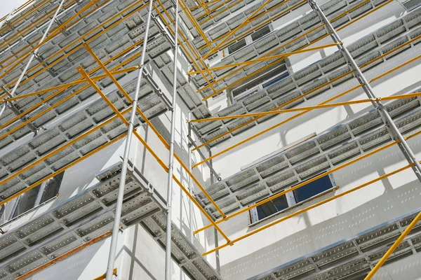 Andaimes perto de uma nova casa, construção exterior, construção e indústria de reparação, parede branca e janela, tubo amarelo — Fotografia de Stock