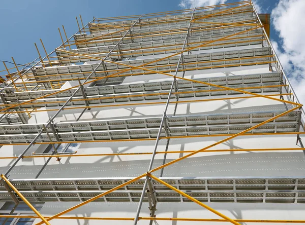 Andamios cerca de una nueva casa, edificio exterior, industria de la construcción y reparación, pared blanca y ventana, tubería amarilla — Foto de Stock