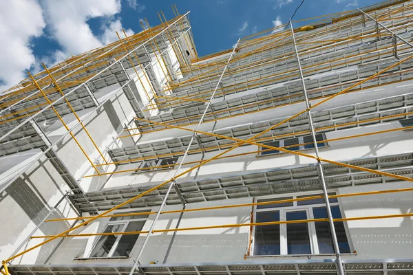 Scaffolding near a new house, building exterior, construction and repair industry, white wall and window, yellow pipe — Stock Photo, Image