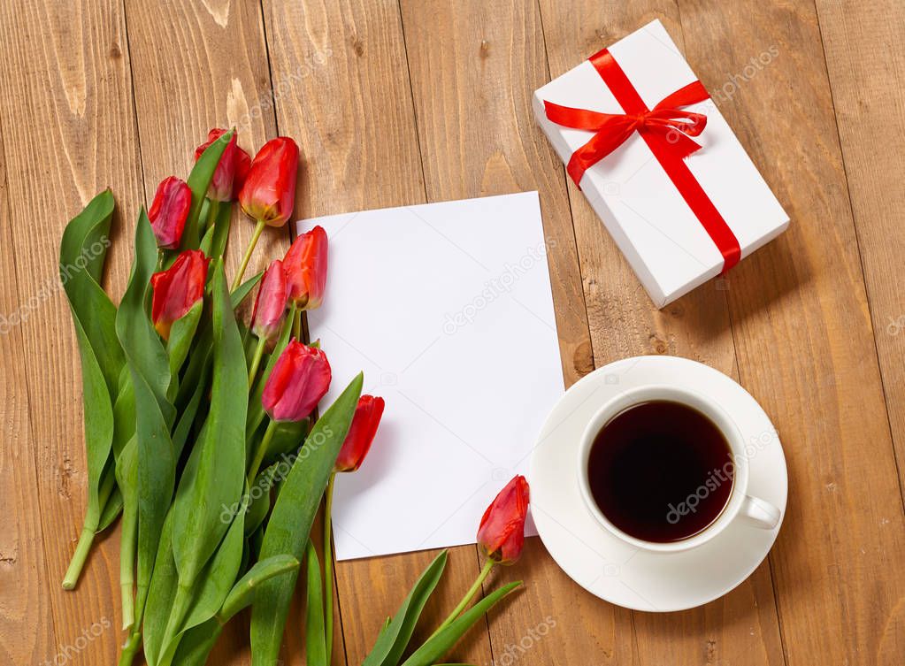 tulips are on wooden boards, cup of coffee, blank paper sheet and gift, greeting concept