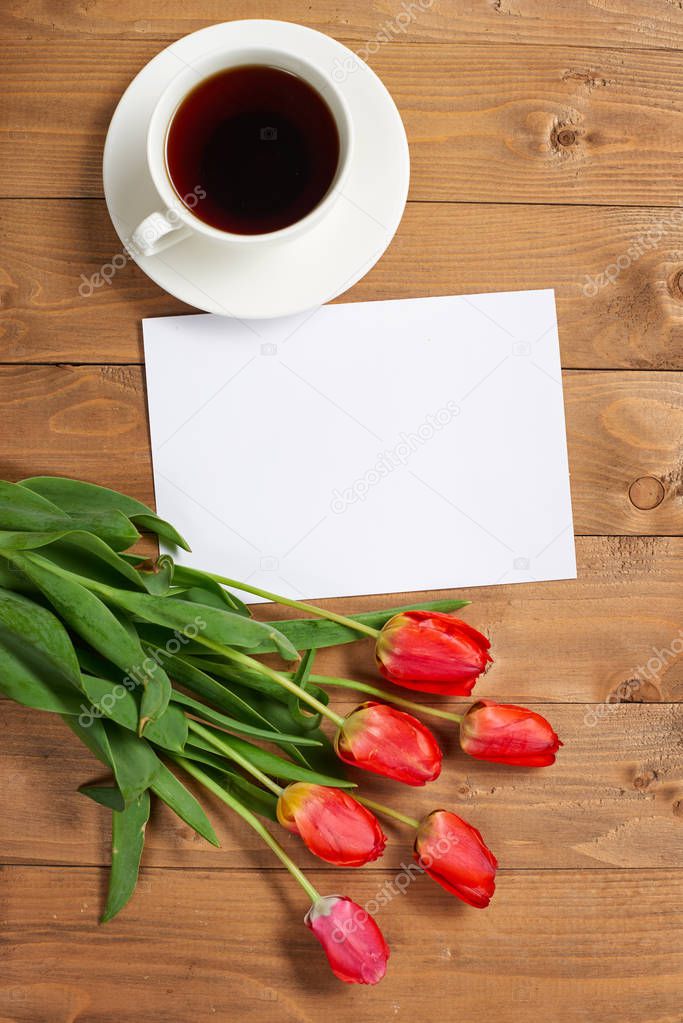 tulips are on wooden boards, cup of coffee, blank paper sheet with place for text - holiday and greeting concept