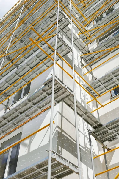 Byggnadsställningar nära ett nytt hus, bygga exteriör, byggande och reparation industrin, vit vägg och fönster, gula röret — Stockfoto