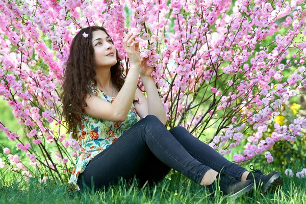 Portré, fiatal lány ült közelében bush rózsaszín virágok — Stock Fotó
