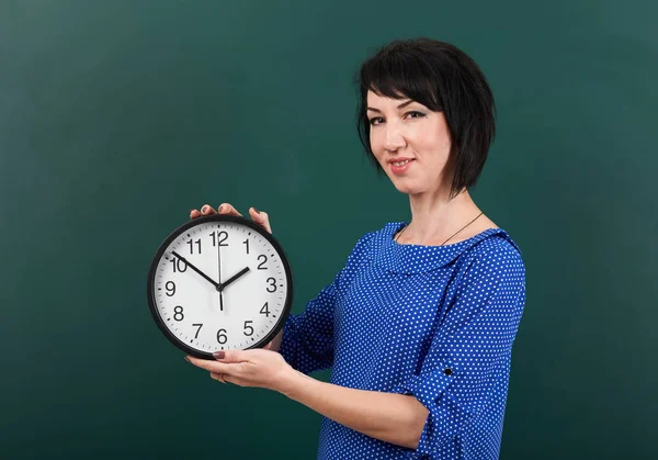 Woman student with big clock posing by chalk Board, education concept, green background, studio shot — Stock Photo, Image