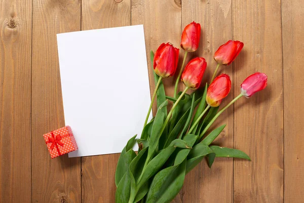 Tulpen zijn op houten planken, blanco papier vel met plaats voor tekst, een klein cadeautje, groet concept — Stockfoto