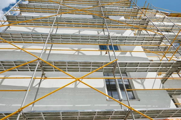 Gerüste in der Nähe eines neuen Hauses, Gebäude außen, Bau- und Reparaturindustrie, weiße Wand und Fenster, gelbes Rohr — Stockfoto