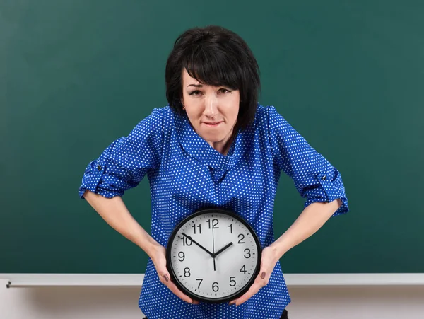 Mujer levanta un reloj pesado, posando por pizarra, tiempo y concepto de educación, fondo verde, toma de estudio — Foto de Stock