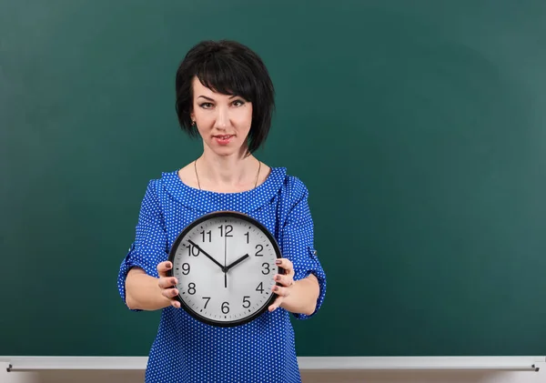 Frau mit großer Uhr posiert mit Kreidetafel, Zeit- und Bildungskonzept, grüner Hintergrund, Studioaufnahme — Stockfoto