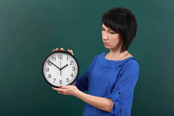 Frau mit großer Uhr posiert mit Kreidetafel, Zeit- und Bildungskonzept, grüner Hintergrund, Studioaufnahme — Stockfoto