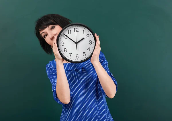 Mujer con gran reloj posando por pizarra, tiempo y concepto de educación, fondo verde, plano de estudio — Foto de Stock