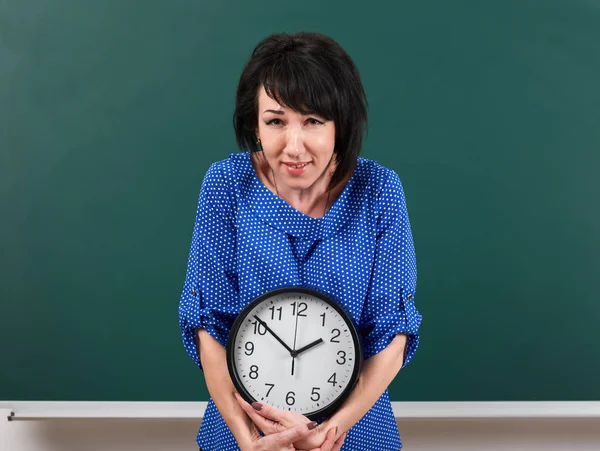 Mujer levanta un reloj pesado, posando por pizarra, tiempo y concepto de educación, fondo verde, toma de estudio — Foto de Stock