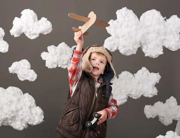 Αγόρι ντυμένος σαν ένα αεροπλάνο πιλοτικά στέκεται ανάμεσα στα σύννεφα και να παίζει με το χειροποίητο αεροπλάνο — Φωτογραφία Αρχείου