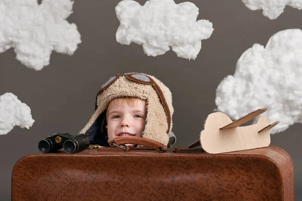Αγόρι ντυμένος σαν ένα αεροπλάνο πιλοτικά κάθονται μεταξύ τα σύννεφα με παλιά βαλίτσα και να παίζει με το χειροποίητο αεροπλάνο — Φωτογραφία Αρχείου